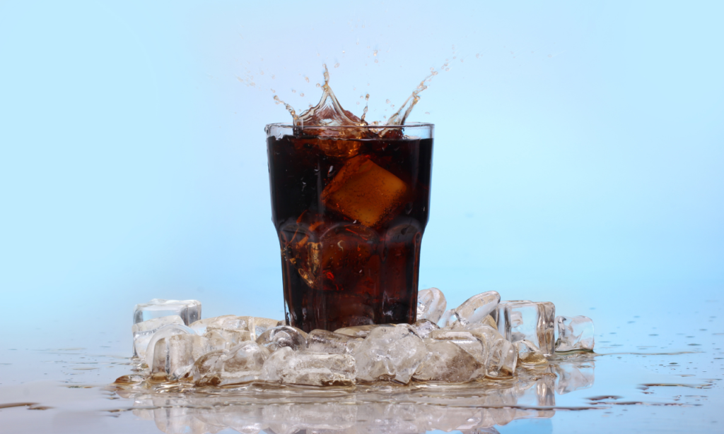 A glass of Coke Zero with ice cubes splashing, surrounded by ice on a reflective surface. The background is a light blue, giving a refreshing, chilled vibe, ideal for conveying the idea of a cold drink