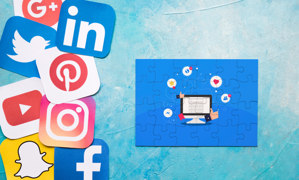 A collection of popular social media icons, including LinkedIn, Twitter, Pinterest, Instagram, Snapchat, YouTube, and Facebook, arranged on a textured blue background. Next to them is a puzzle piece showing an illustration of a person working on a laptop, surrounded by various social media symbols like hearts, notifications, and user icons, signifying social media interaction and marketing